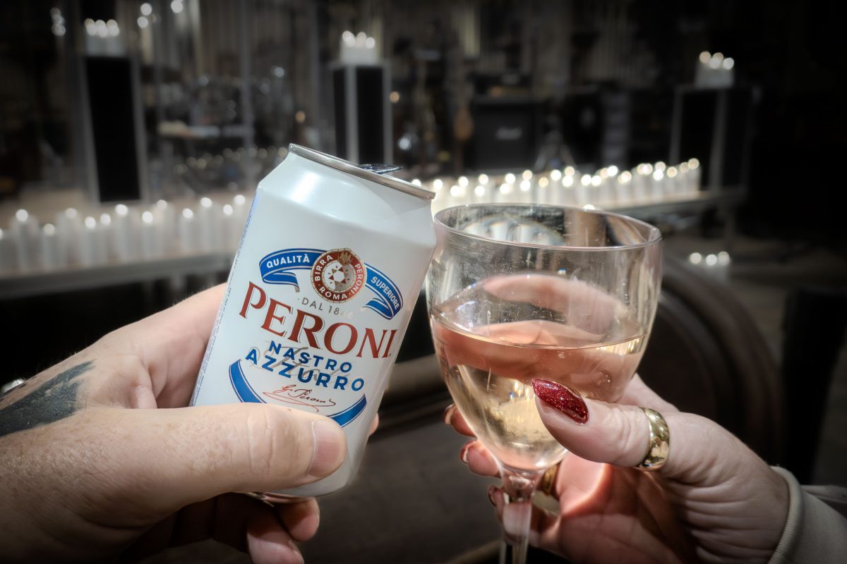 Couple toasting with a can of Peroni and a glass of wine surrounded by candles as they watch the Oasis tribute band performing by candlelight at derby cathedral