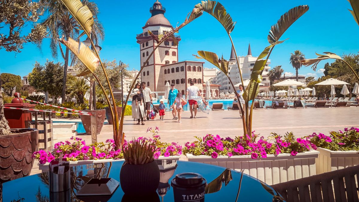 Families walking by the pool area at the Titanic Mardan Palace in Antalya with the iconic lighthouse tower in the background