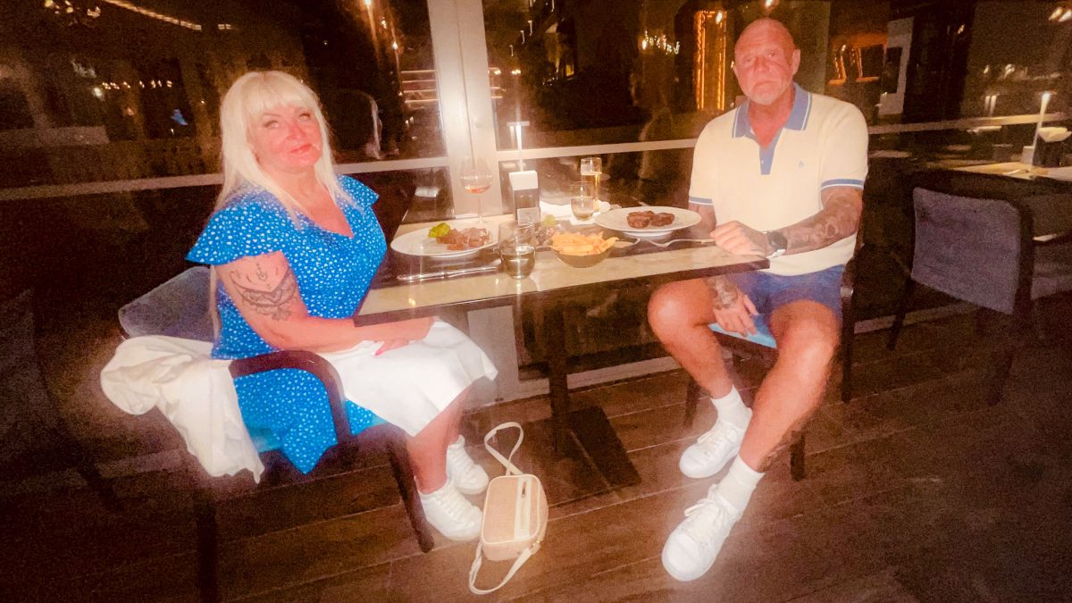 Two diners seated at an outdoor terrace table at Titanic Mardan Palace, enjoying a meal with steak, fries and drinks in a softly lit night-time setting