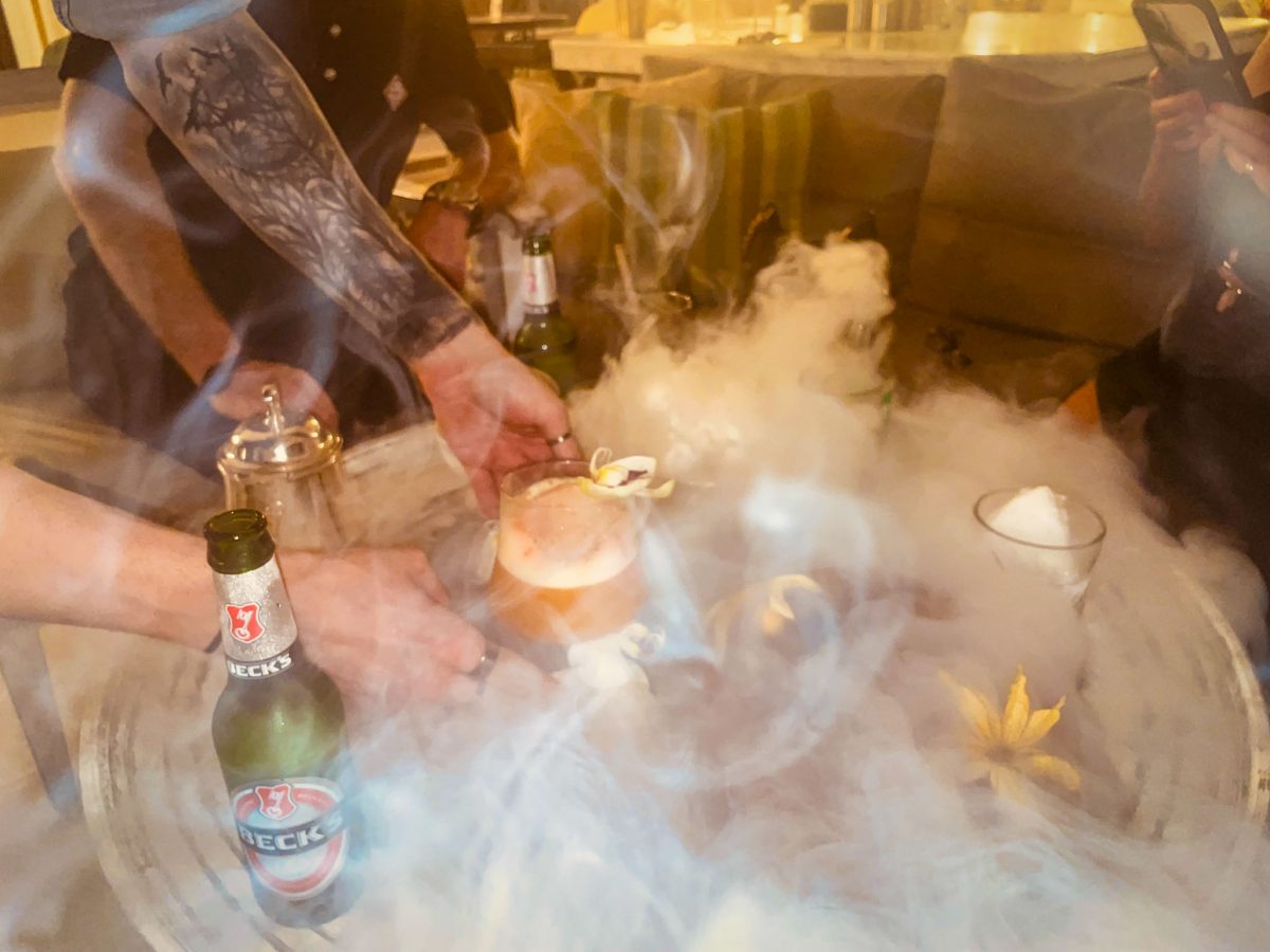 A bartender presenting a smoky cocktail surrounded by dramatic dry ice vapour on a table with drinks at Titanic Mardan Palace