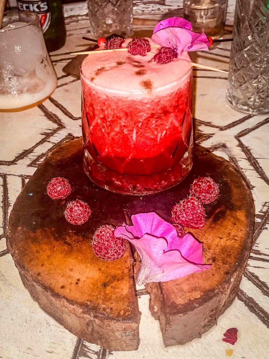 A vibrant raspberry cocktail served on a rustic wooden board, decorated with fresh raspberries and a pink flower at Titanic Mardan Palace