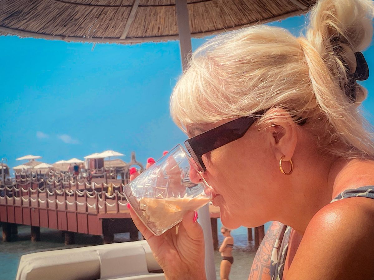 Woman enjoying a drink while relaxing by the beach with a wooden pier and sun umbrellas in the background at Titanic Mardan Palace