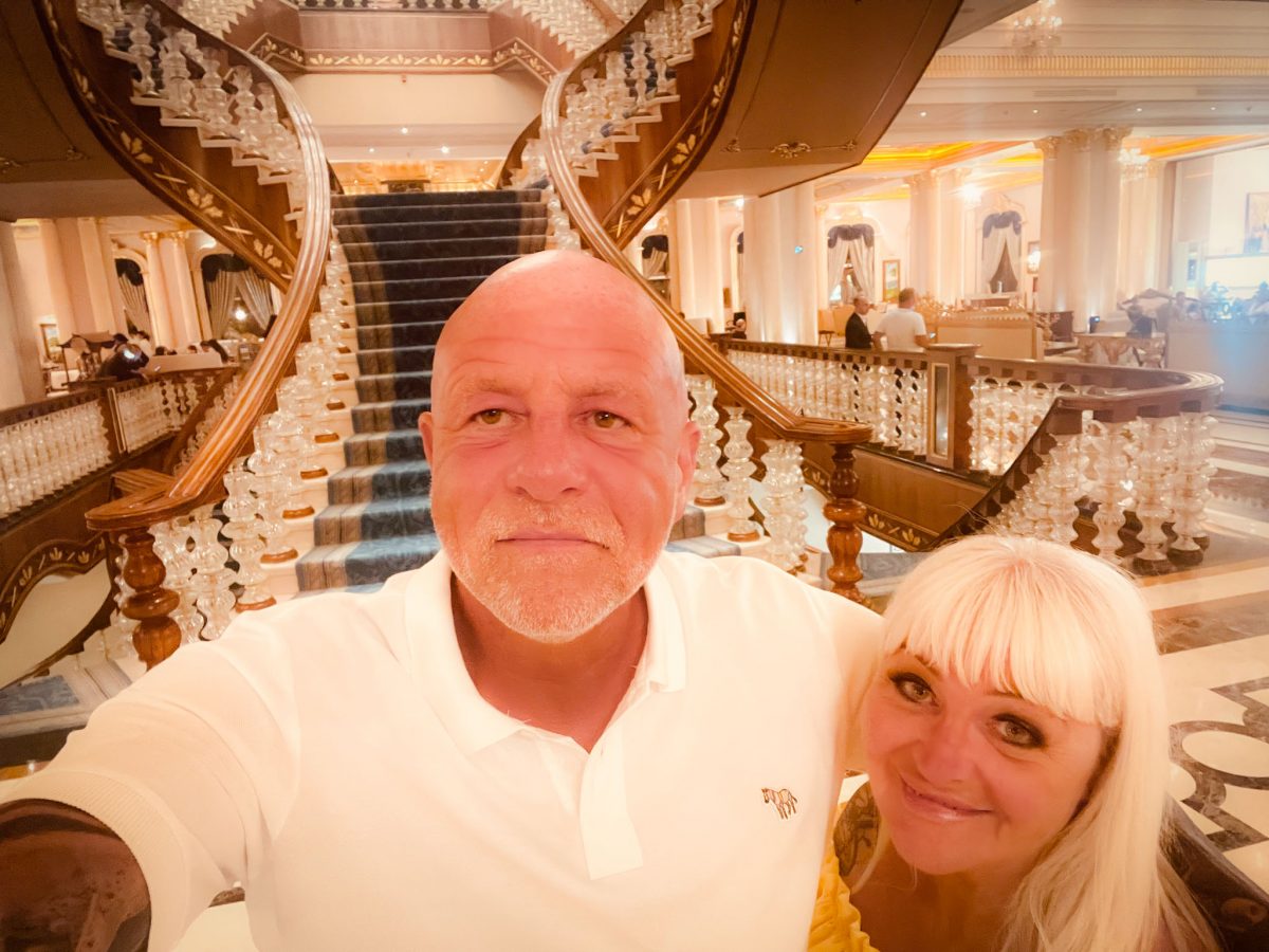 Couple taking a selfie in front of the grand staircase inside the elegant lobby of Titanic Mardan Palace in Antalya