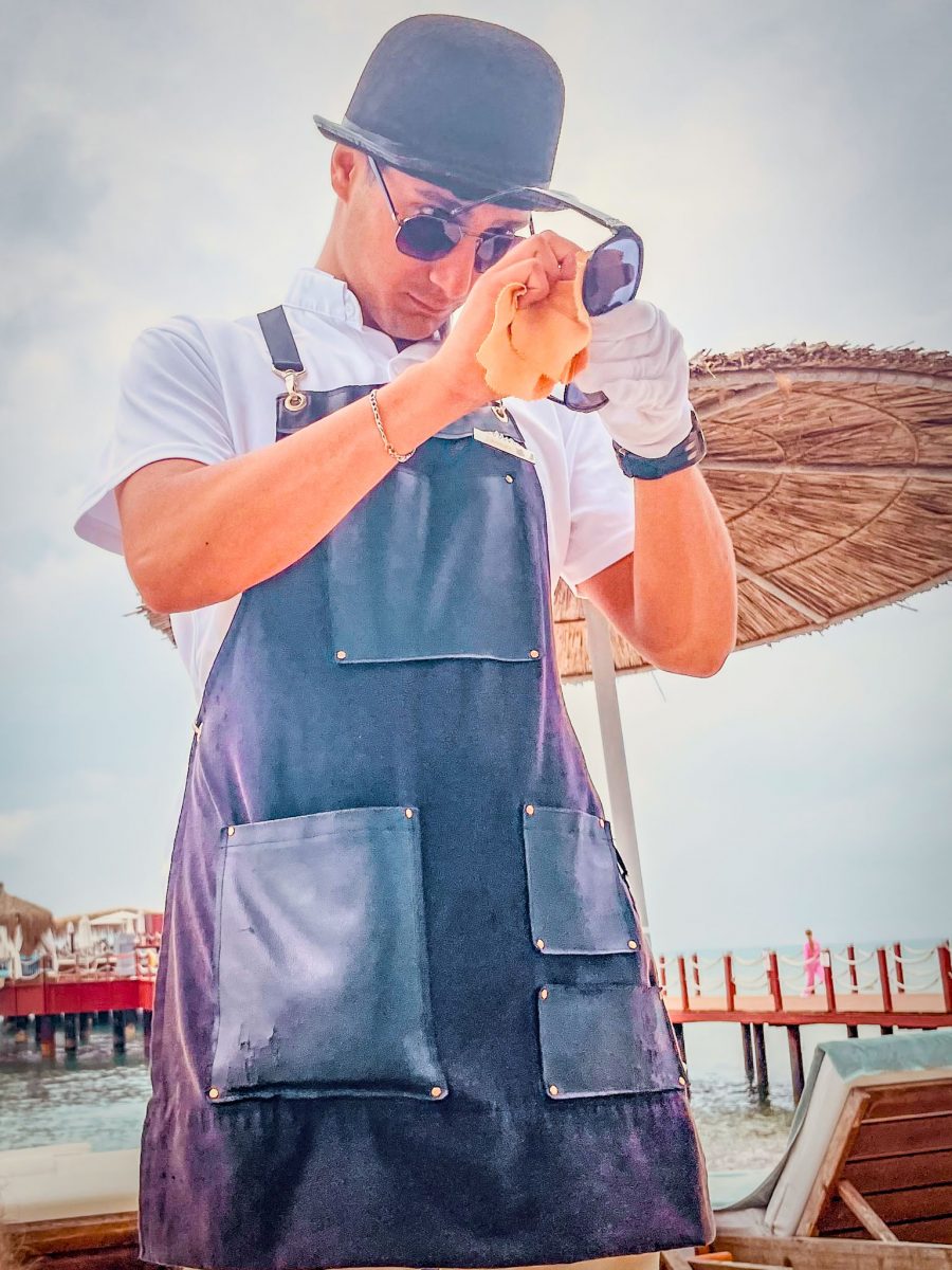A staff member at Titanic Mardan Palace cleaning a guest’s sunglasses while standing by the beach and pier