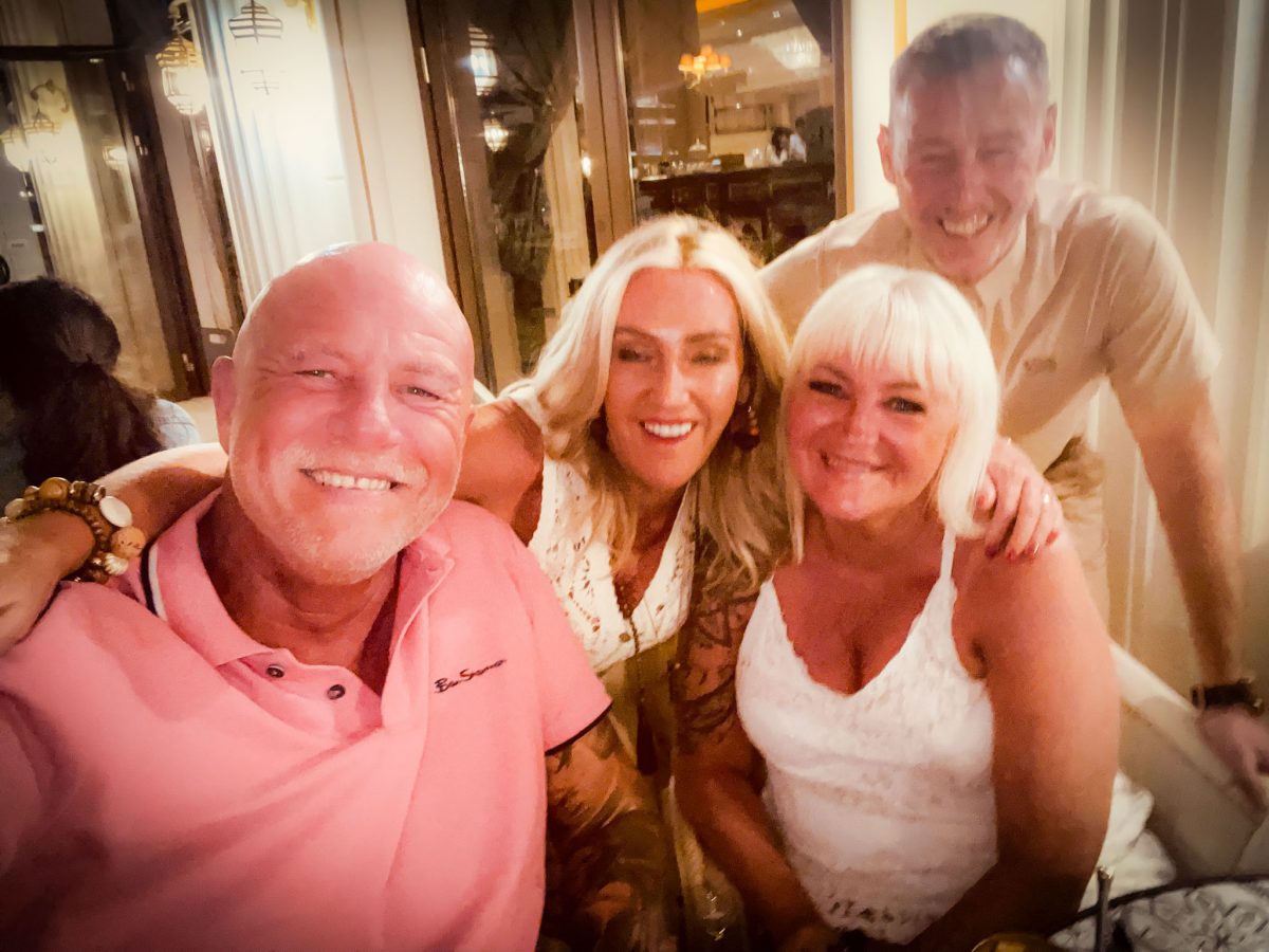 Four friends smiling and posing together at a warmly lit restaurant during the evening.