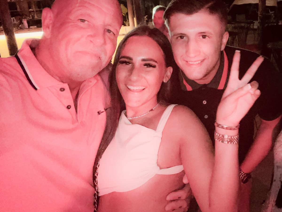 Three friends smiling and posing together at a night-time venue with warm red lighting.