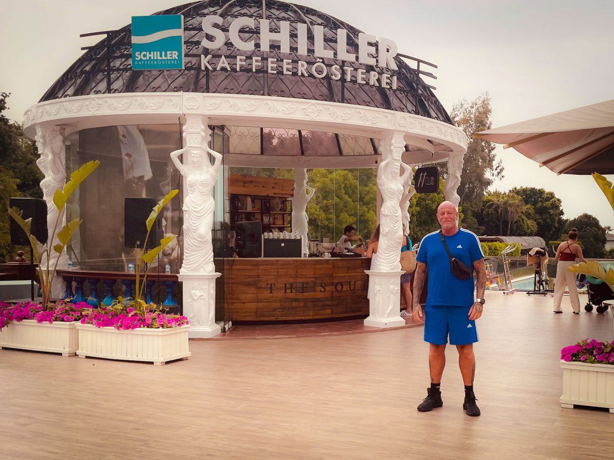 A man standing on the outdoor terrace of Schiller Kaffee Rösterei at a luxury resort in Antalya, with the café's white sculpted columns and dome behind him.