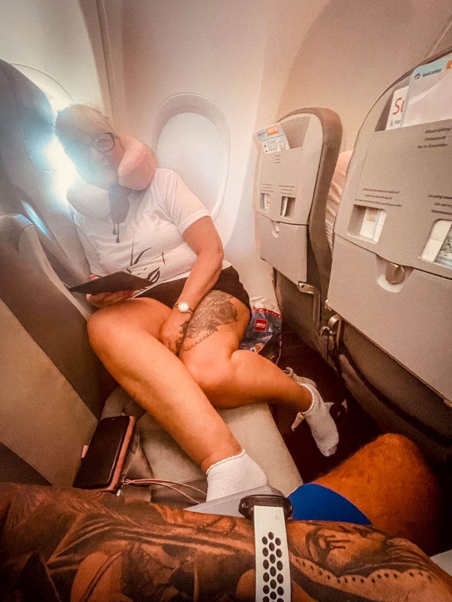 Passenger resting on an airplane seat with a travel pillow, tablet, and personal items during a flight.