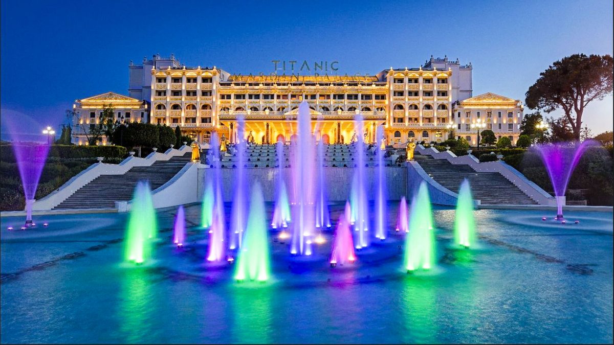 Colourful illuminated fountains in front of the Titanic Mardan Palace hotel at night.