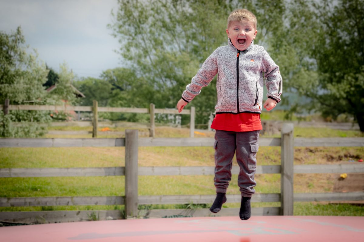 A young boy jumping high in the air on a large, pink bouncing pillow at Amerton Farm.