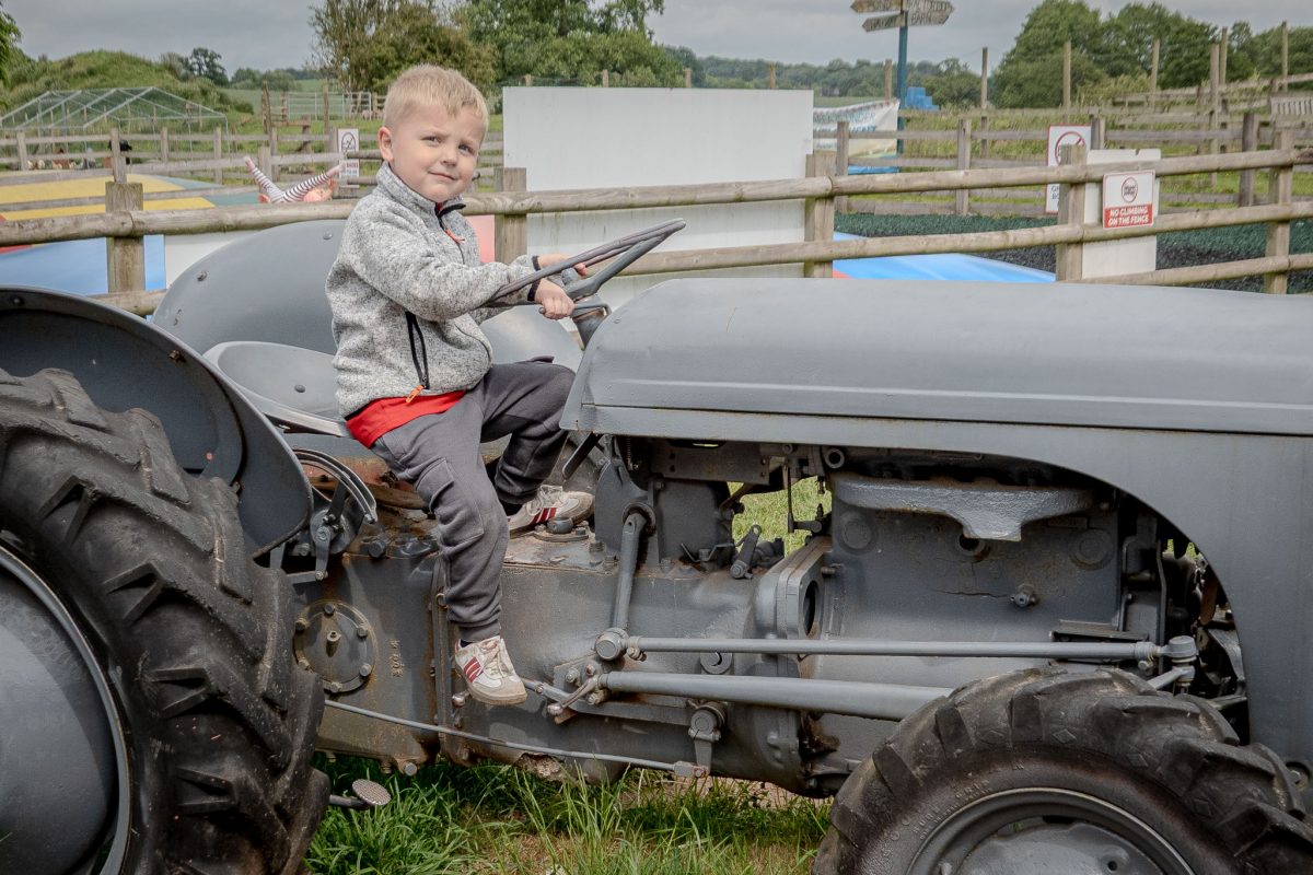 A young boy sitting on the seat of an old grey vintage tractor, pretending to drive.