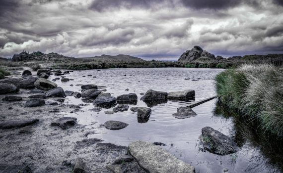 Moody landscape of Doxey Pool at The Roaches in the Peak District, featuring dark water, scattered rocks and stormy skies.
