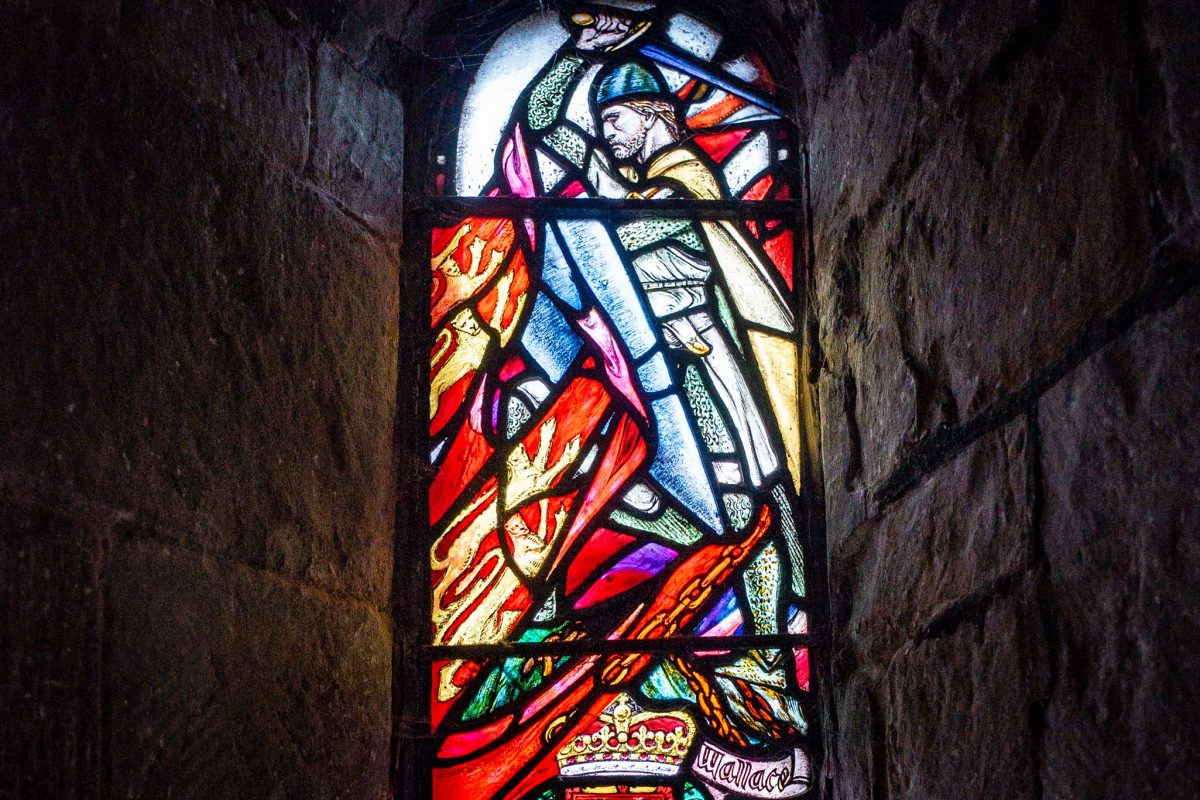 A vibrant stained glass window depicting a historical figure, likely William Wallace or Robert the Bruce, in armor and holding a sword.
