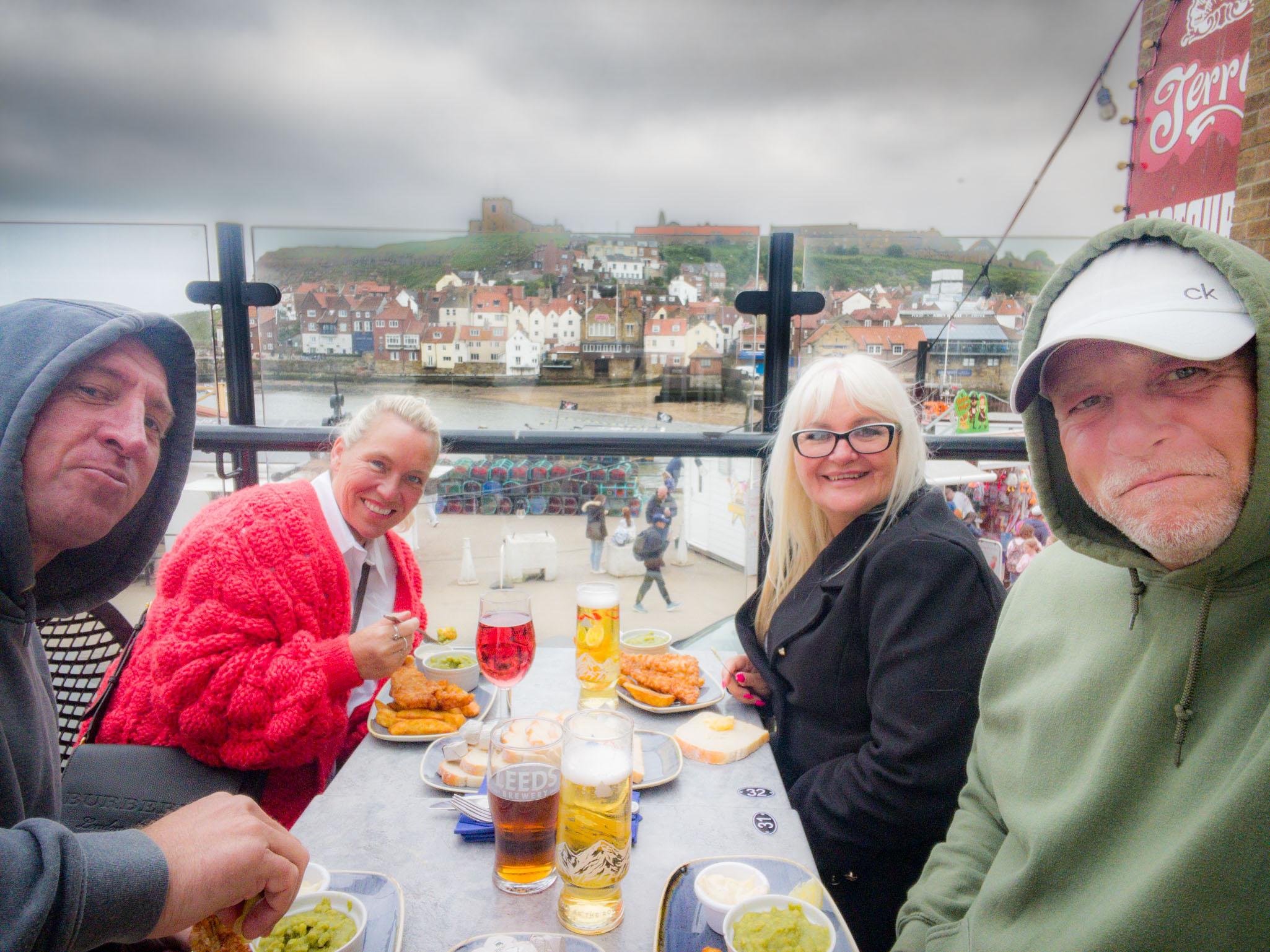 Four people eating fish and chips with a view of the colorful houses of Whitby across the water from the patio of The Pier Inn.