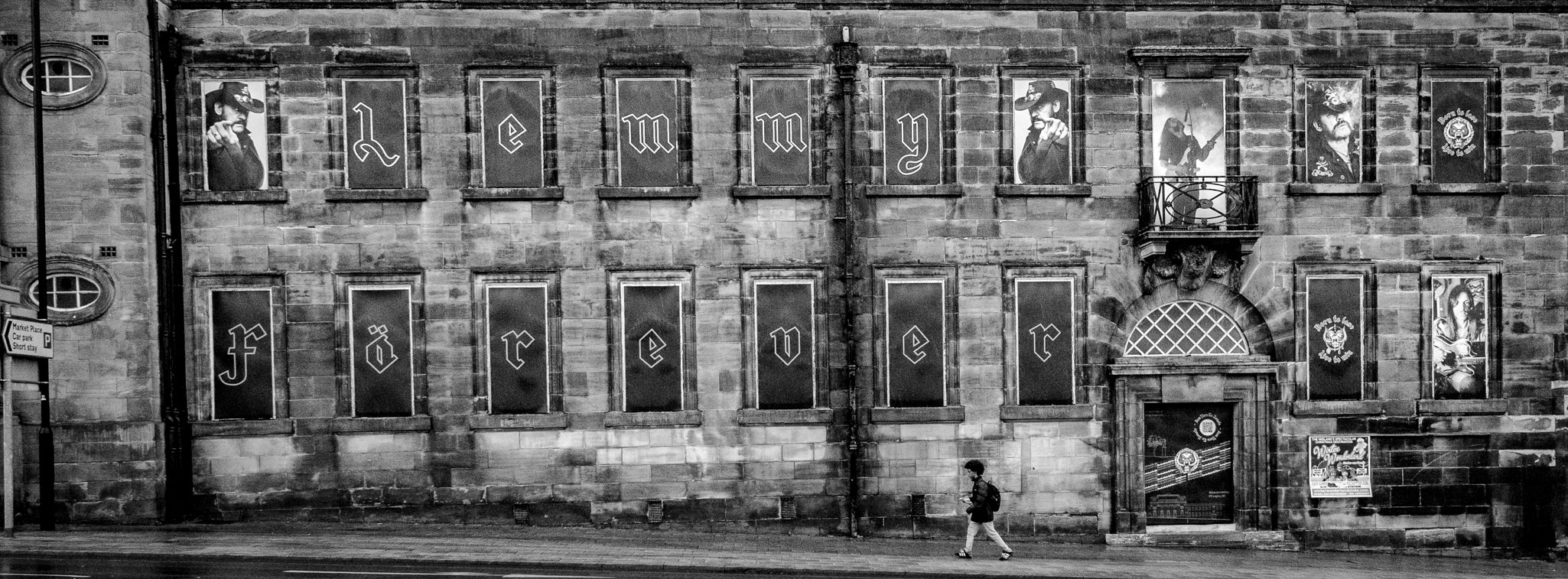 A wide, monochrome street view of the Former Post Office Building in Burslem featuring a 'Lemmy Forever' tribute in the windows.