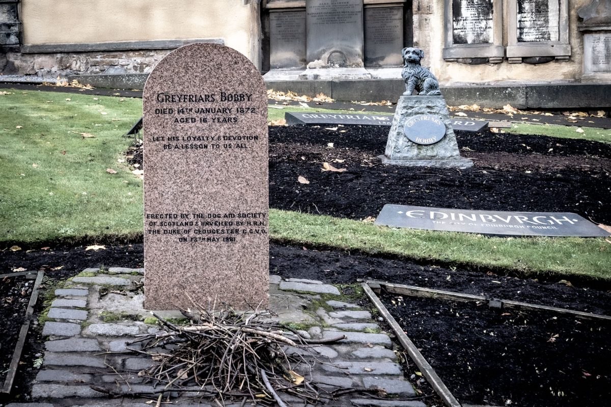 Headstone of Greyfriars Bobby, a loyal Skye Terrier, in Greyfriars Kirkyard, Edinburgh. A small statue of the dog is placed on a stone base behind the grave.