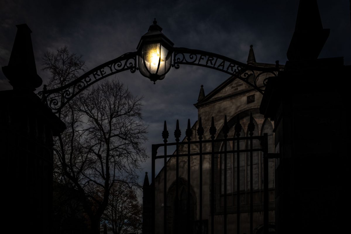 Historic stone entrance gate to Greyfriars Kirkyard cemetery in Old Town Edinburgh, with a view of the path and gravestones inside.