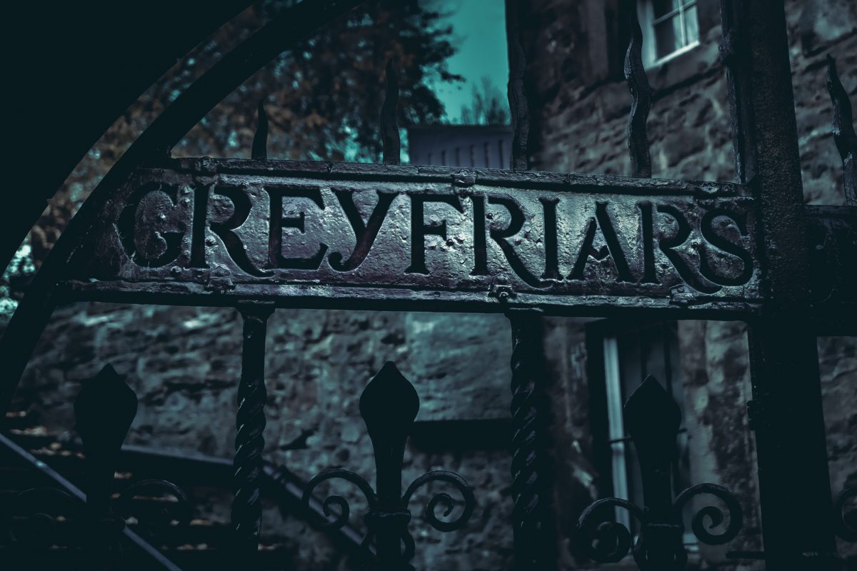 Close-up of the dark, aged iron gates of Greyfriars Kirkyard with the name 'GREYFRIARS' clearly visible in the metalwork.