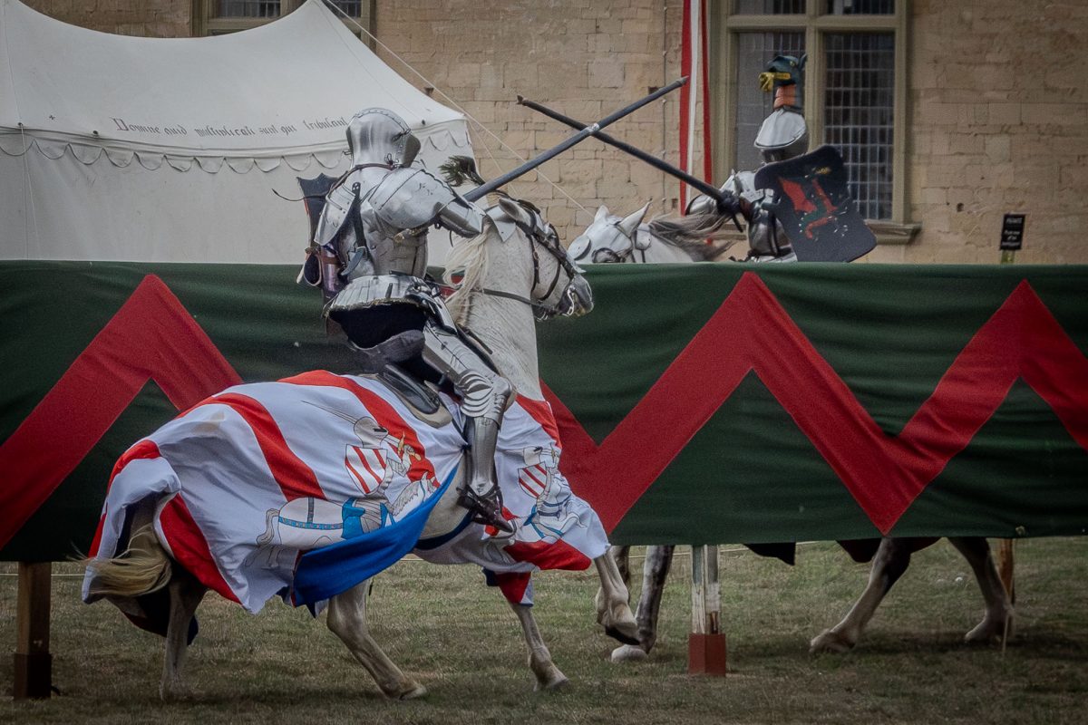 Two knights crossing lances mid-pass during a joust, the knight on the white, barded horse has their lance crossed with the opponent's.