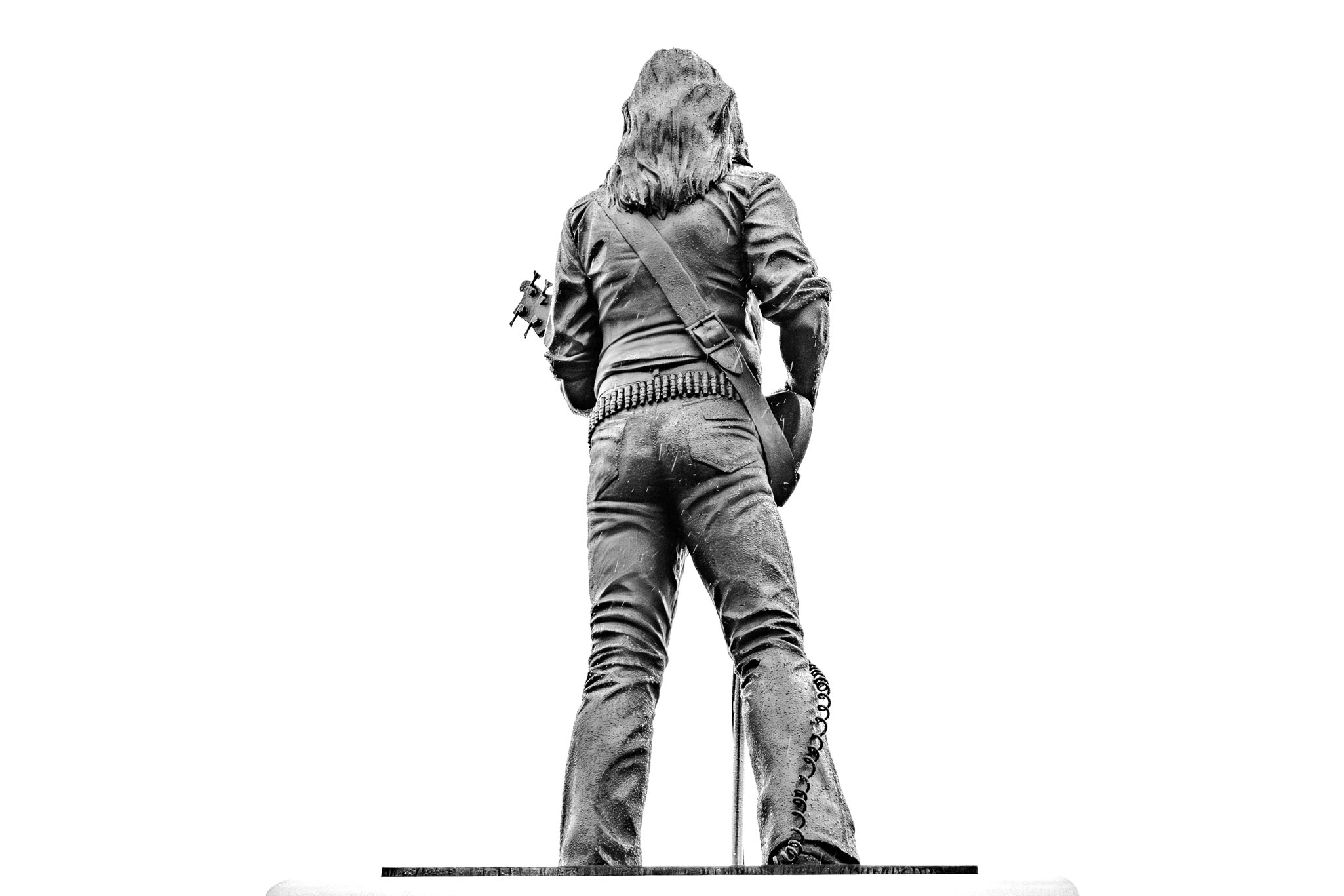 A low-angle, black and white rear view of the Lemmy Kilmister statue, highlighting his bullet belt.