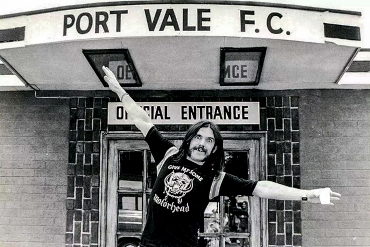 Vintage black and white photo of Lemmy Kilmister standing in front of the Port Vale F.C. stadium entrance.