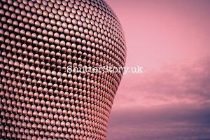 Close-up architectural detail of the curved Selfridges building in Birmingham featuring shimmering silver discs under a pink sky.
