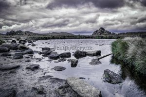A dark, rocky pool of water on a high gritstone ridge under heavy, dramatic storm clouds in the Peak District.