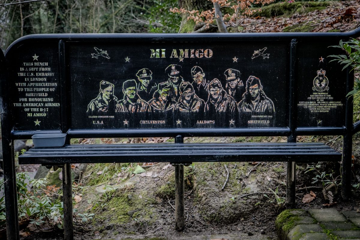 A black metal bench featuring an etched illustration of the ten airmen and the text 'Mi Amigo' with descriptions of their mission.