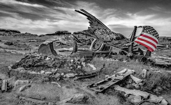 Black and white photo of the wreckage of a military aircraft on the barren moors near Glossop, UK. A small American flag, partially colorised in red and white stripes, is attached to the debris.