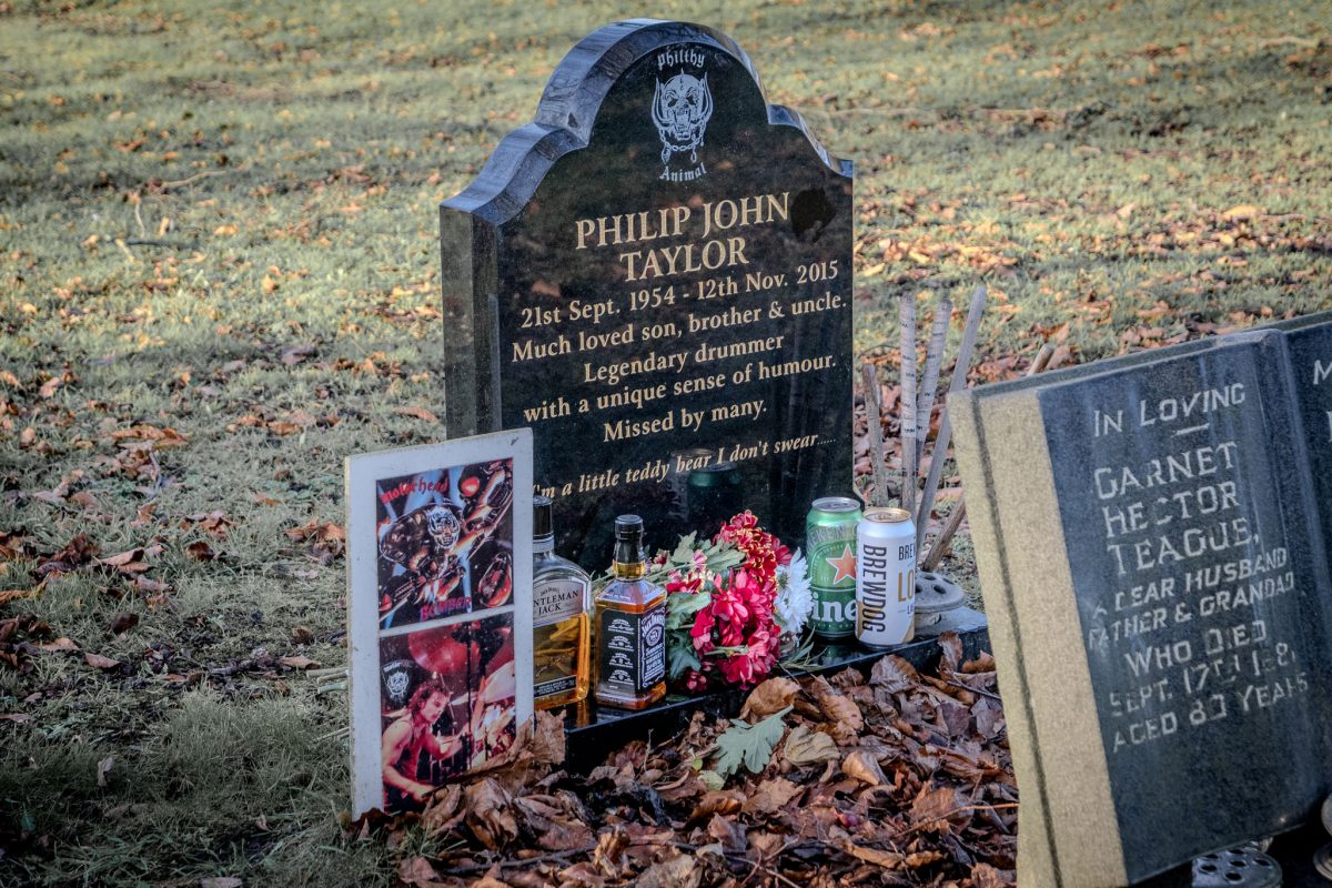 Medium shot of Phil Taylor's headstone with bottles of whiskey, beer, and photo.