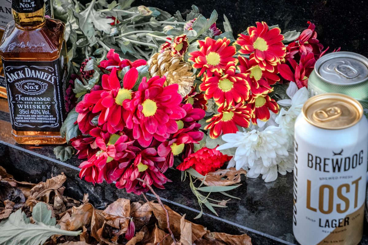 Close-up of Jack Daniel's bottle, red flowers, and BrewDog can at the grave.
