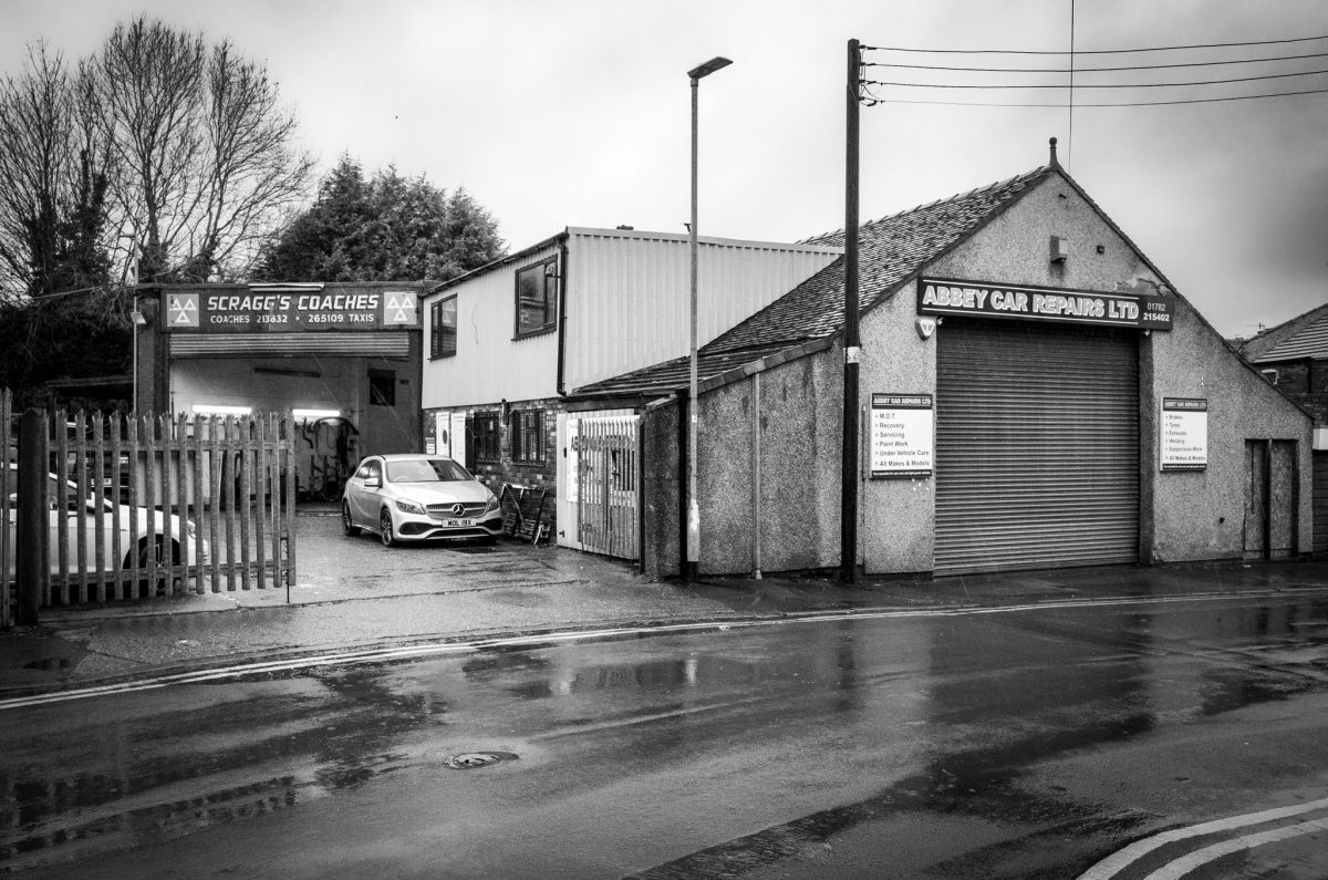 A black and white street view of a two-story commercial building with signage for Scragg's Coaches and Abbey Car Repairs under a grey sky.