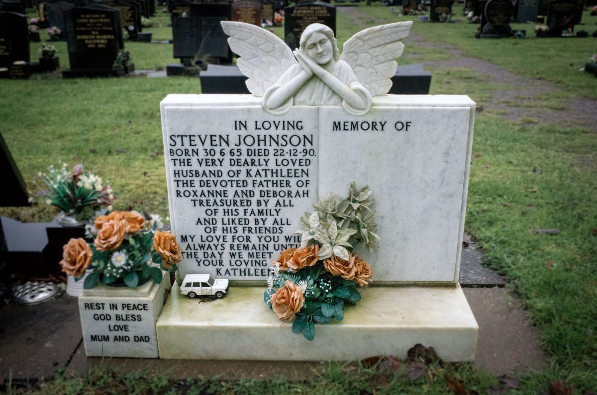 A white marble grave memorial for Steven Johnson with a carved angel and a small toy taxi on the base.