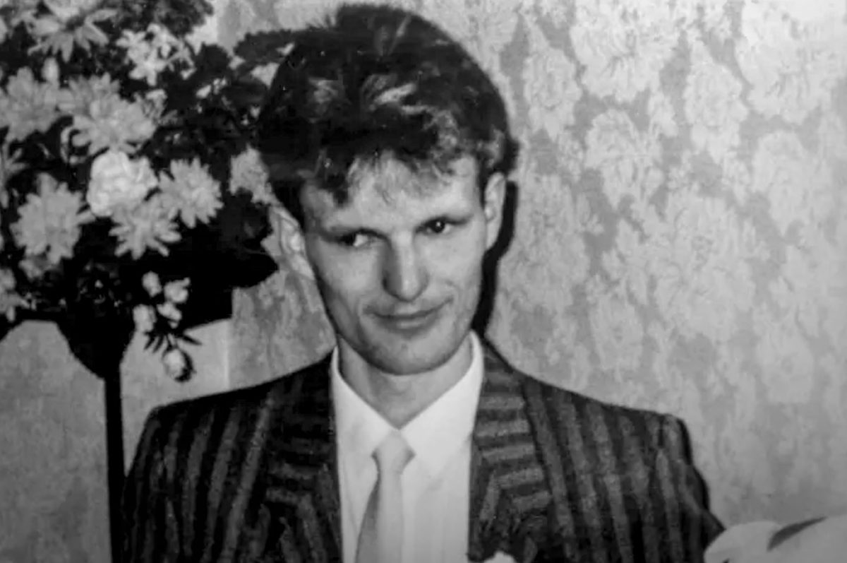 A black and white candid portrait of a young man with dark hair in a suit with a tie possibly at a wedding