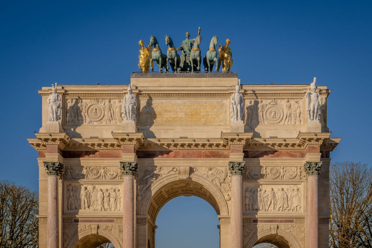 Close-up of the Arc de Triomphe du Carrousel featuring the golden chariot statue against a clear blue sky in Paris.
