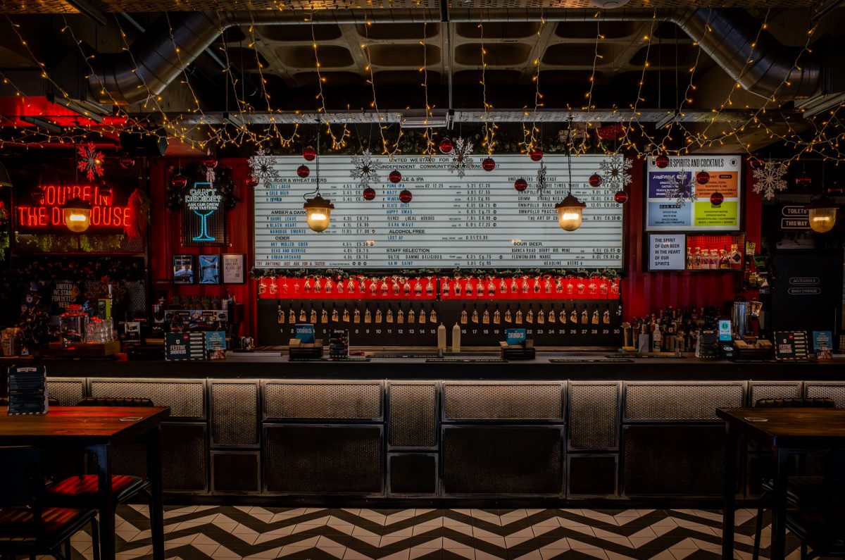 Interior view of the BrewDog DogHouse Manchester bar with a long row of beer taps and neon signage.