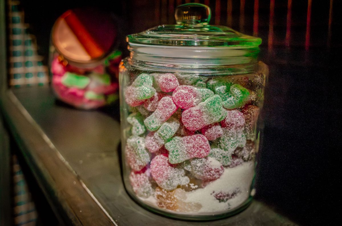 A glass jar filled with green and red gummy sweets on a shelf.