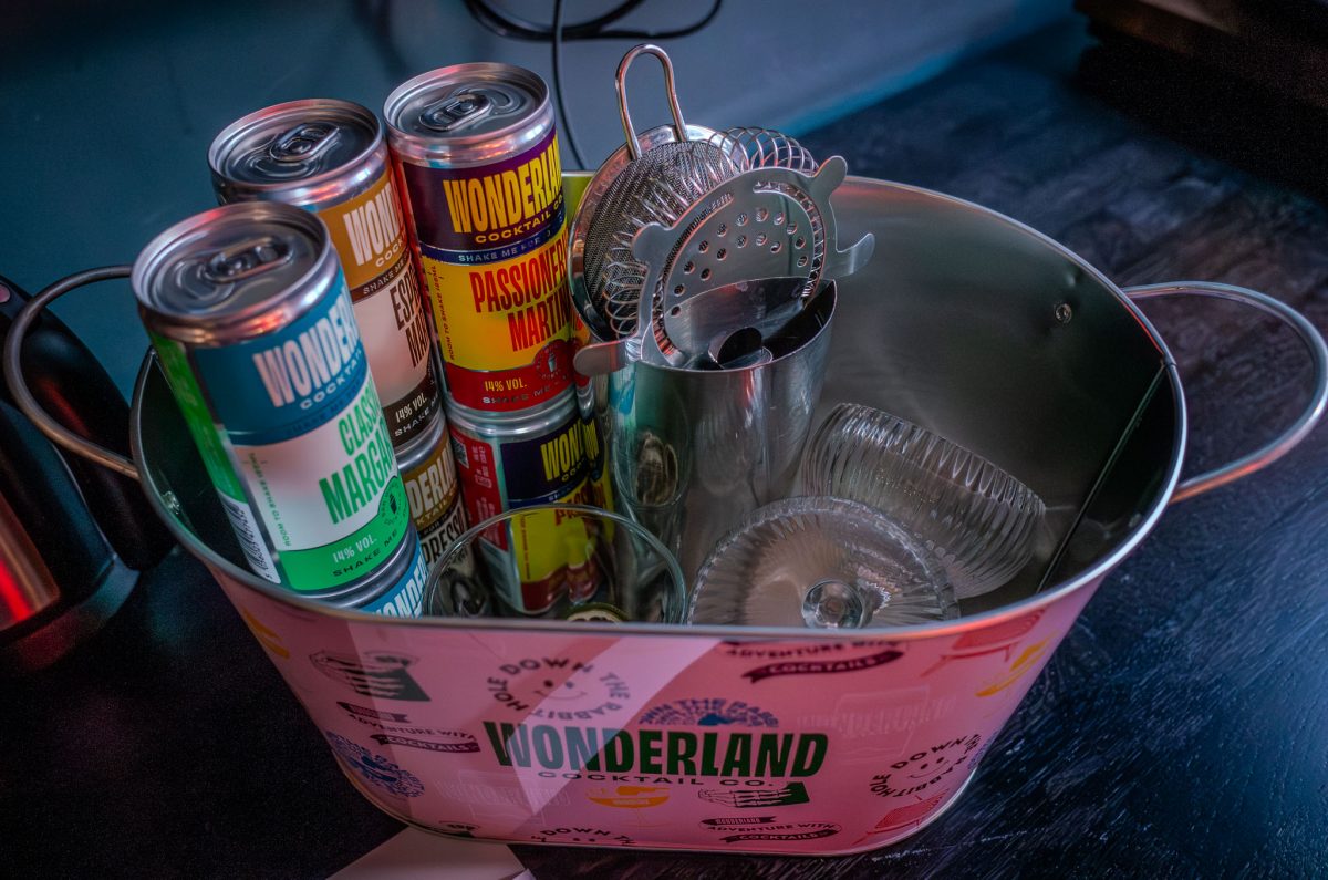 An ice bucket containing canned margaritas and martinis alongside a cocktail shaker and strainer.