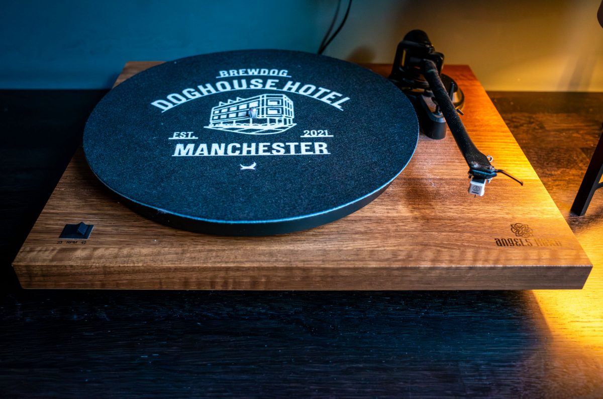 Close-up of a wooden record player with a black slipmat that reads BrewDog DogHouse Hotel Manchester.