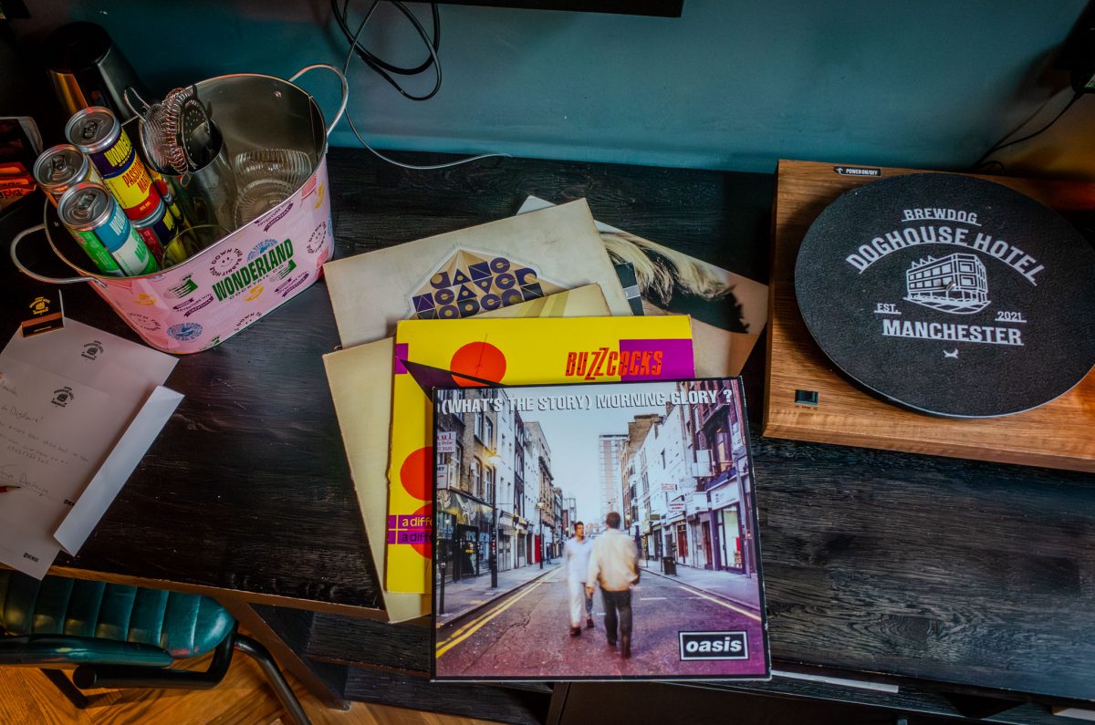 A desk featuring a record player, vinyl records including Oasis Morning Glory, and a cocktail bucket.