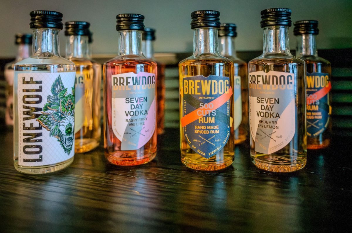 Small glass bottles of BrewDog branded spirits lined up on a dark wooden surface.