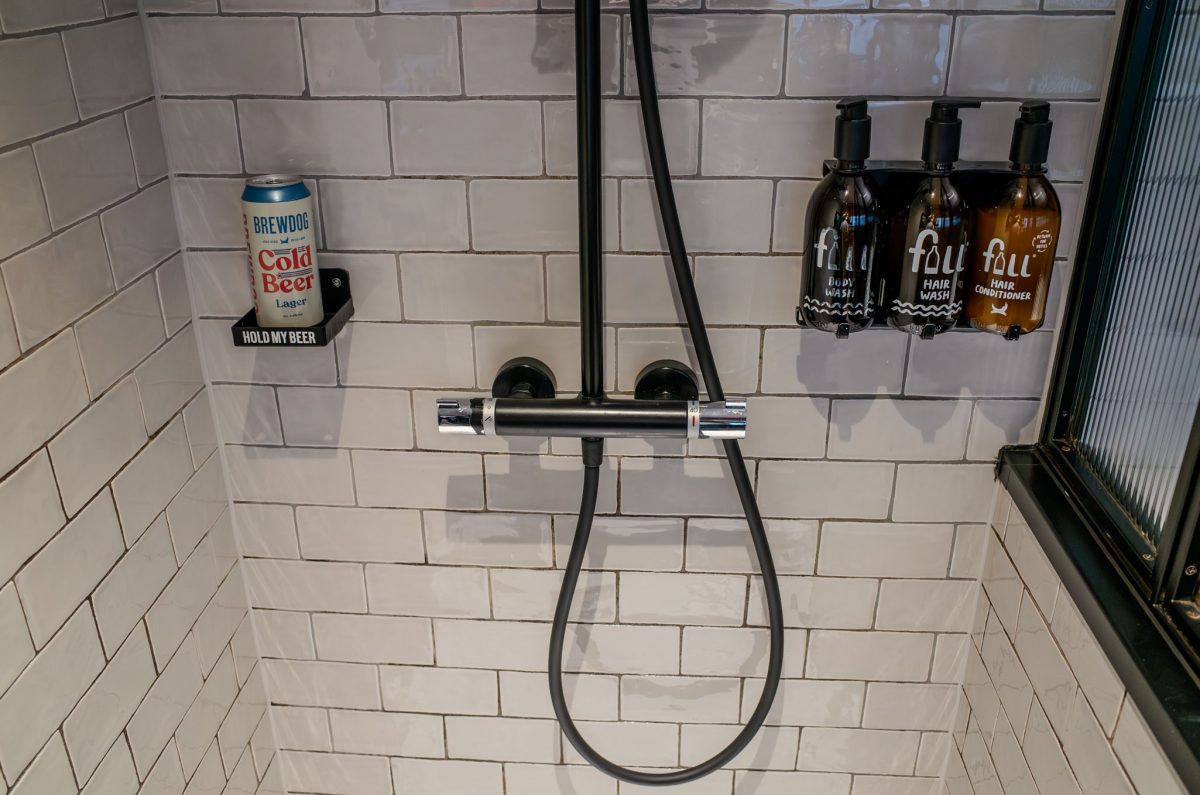 A shower wall with a can of BrewDog beer in a holder next to bottles of hair and body wash.