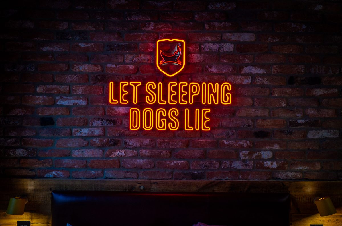 A red neon sign with a dog logo and the text Let Sleeping Dogs Lie on a brick wall.