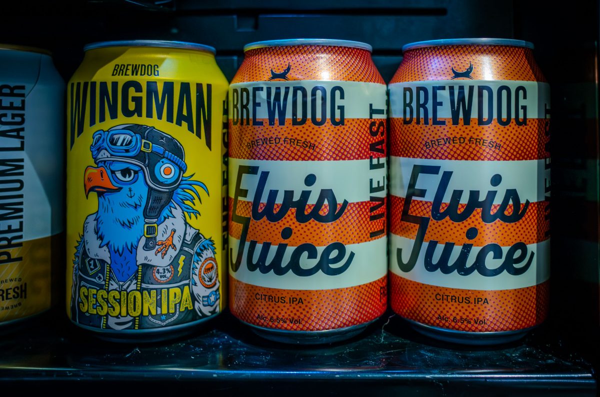 Three cans of BrewDog beer, including Wingman Session IPA and Elvis Juice Citrus IPA, sitting on a shelf.