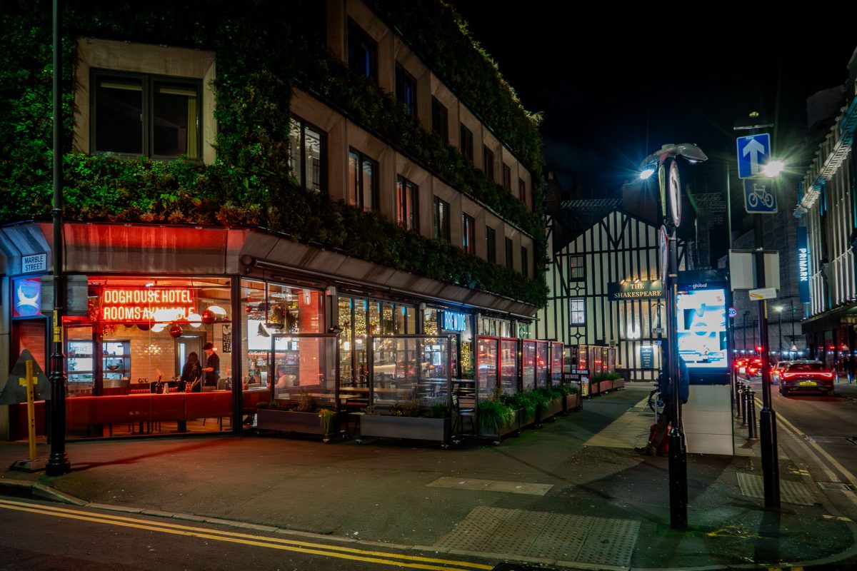 Exterior view of the BrewDog DogHouse Manchester hotel and bar at night with bright neon lights.
