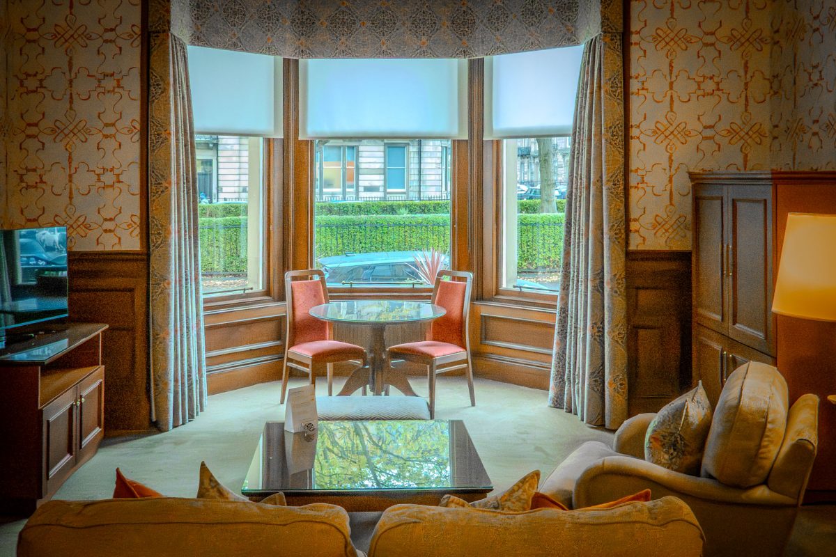 A bright hotel sitting room with a sofa facing a large bay window overlooking an Edinburgh street.