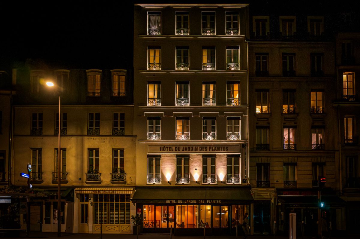 The front of a Parisian hotel at night with warm lights glowing from the windows and entrance.