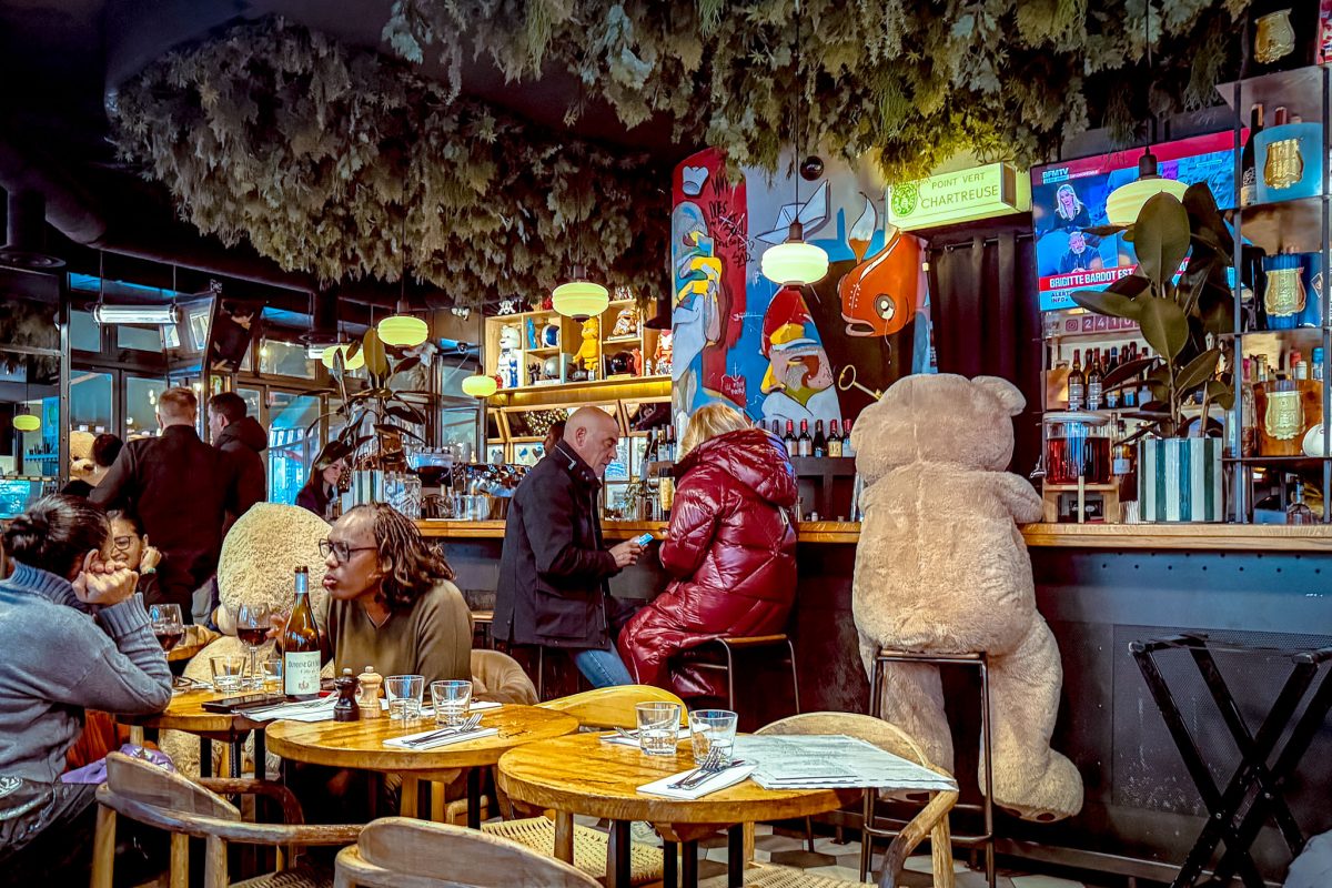 Interior of a Parisian bistro with large teddy bears sitting at the bar and tables.