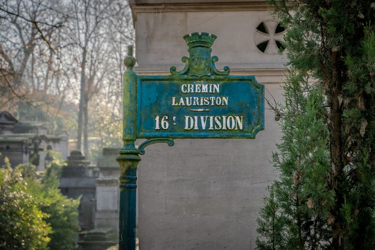 A weathered green and gold street sign for Chemin Lauriston in the 16th Division of Père Lachaise Cemetery.