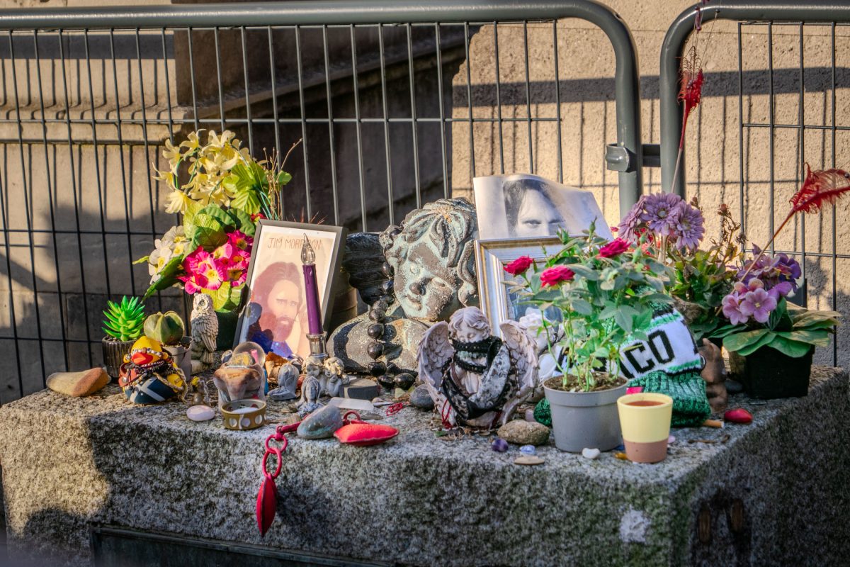 A collection of flowers, photos, figurines, and a purple candle left by fans on top of Jim Morrison's grave.